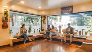 A reception area with a wooden bench seating, potted plants, and a large window offering a view of the outdoors. - Oriva Deccan 8 (Pune)