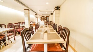Une longue table à manger entourée de chaises, un plafond doté d’un éclairage encastré et un couloir menant à une porte.