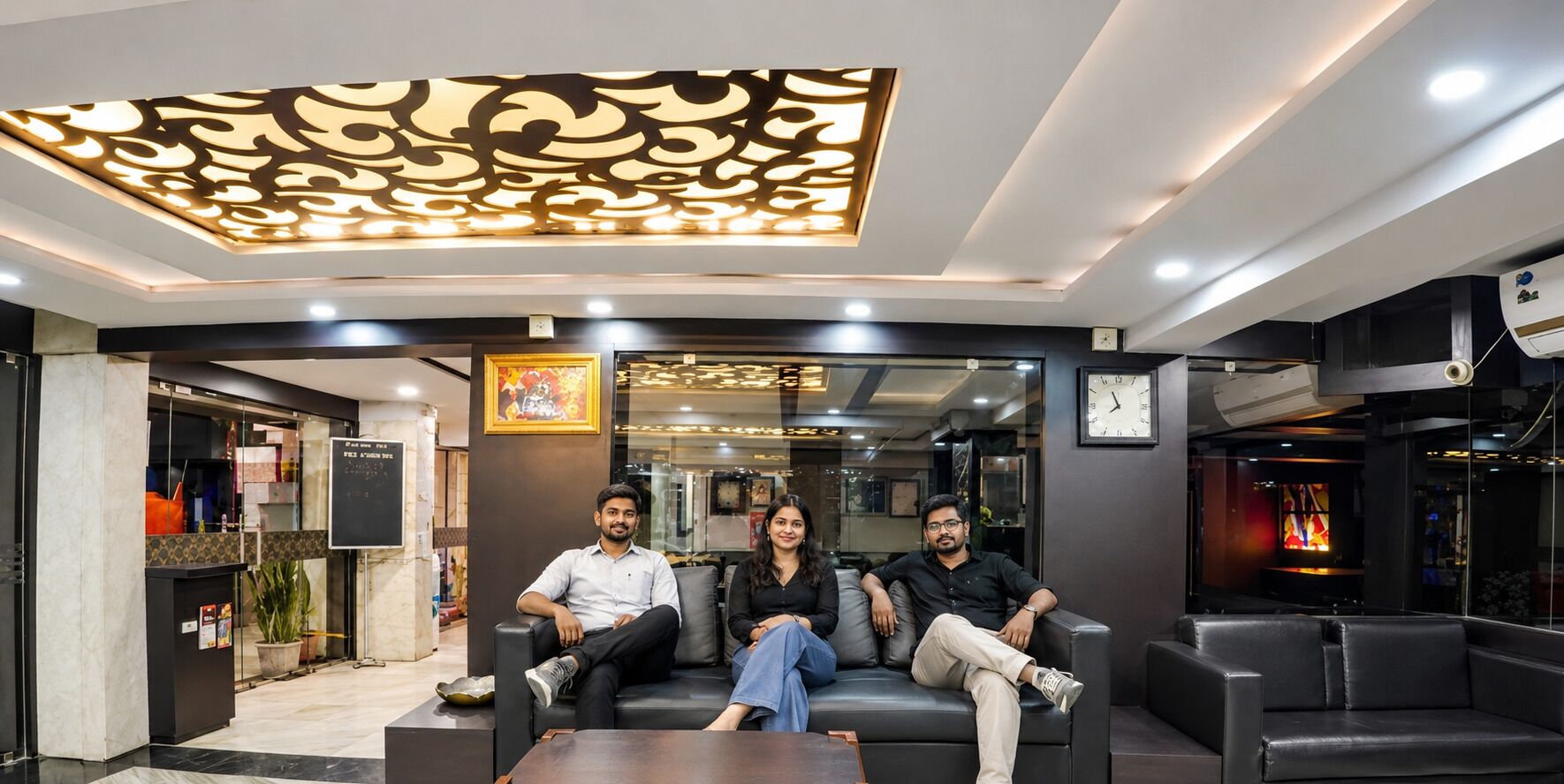 A reception area with a modern ceiling design, a seating area with leather sofas, and a visible clock on the wall.
