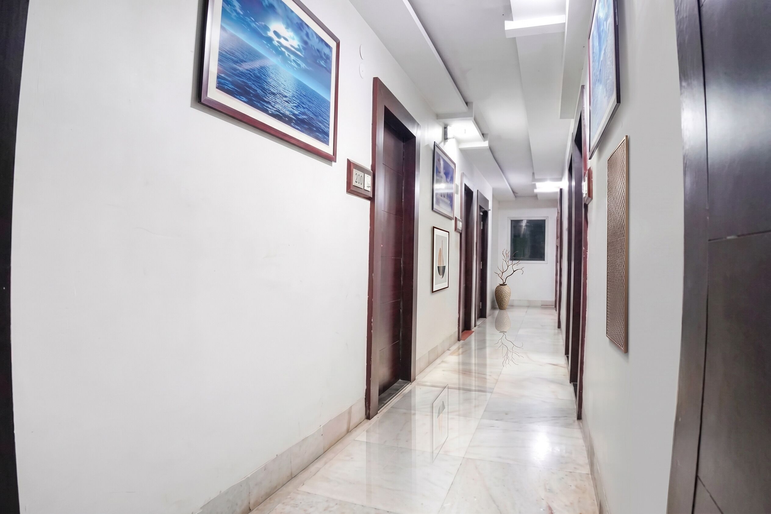Um corredor com piso lustroso, quadros nas paredes e uma porta com o número.