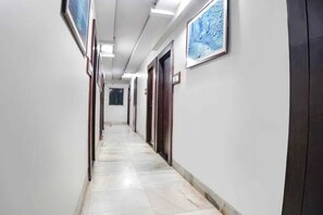 A long, narrow hallway with white walls and tiled flooring, leading to multiple doors.