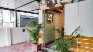 Entrada de hotel con puerta de cristal, plantas en macetas y suelo de baldosas.