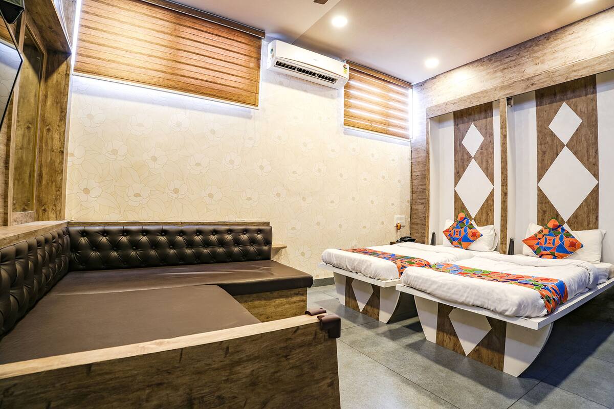Una habitación de hotel moderna con sofá, dos camas, paneles de madera y un equipo de aire acondicionado.