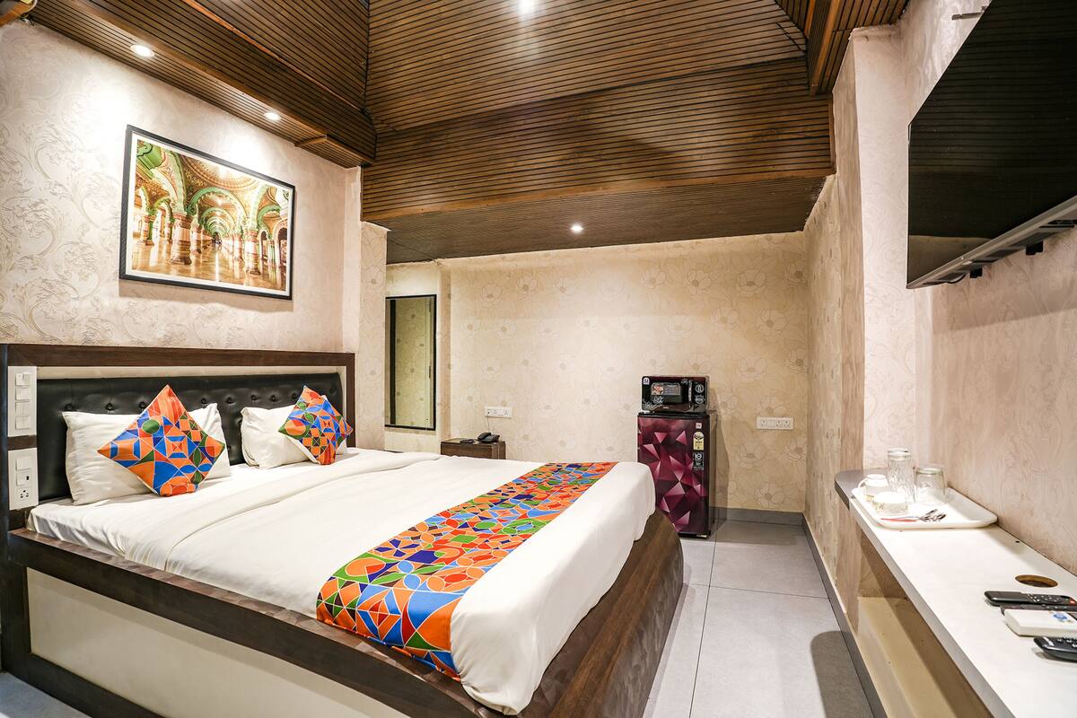 Una habitación de hotel con cama, mesita de noche, cómoda, espejo y televisor montado en la pared.