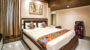 Habitación de hotel con una cama grande, cabecera de madera, colcha colorida, una obra de arte en la pared y un refrigerador.