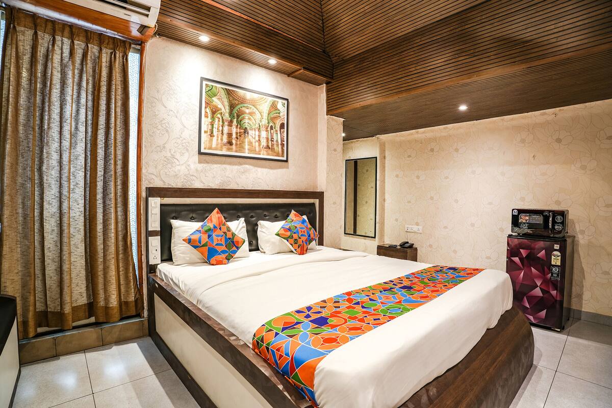 Habitación de hotel con una cama grande, cabecera de madera, colcha colorida, una obra de arte en la pared y un refrigerador.