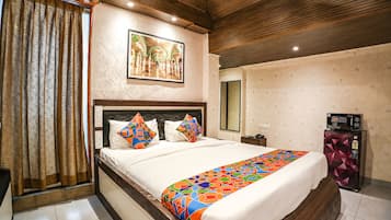 Een hotelkamer met een groot bed, een houten hoofdeinde, een kleurrijk sprei en een kunstwerk aan de muur, plus een koelkast.