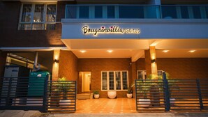 La entrada de Bougainvillea Suites, con fachada de ladrillo, ventanas amplias y un camino de entrada porticado.