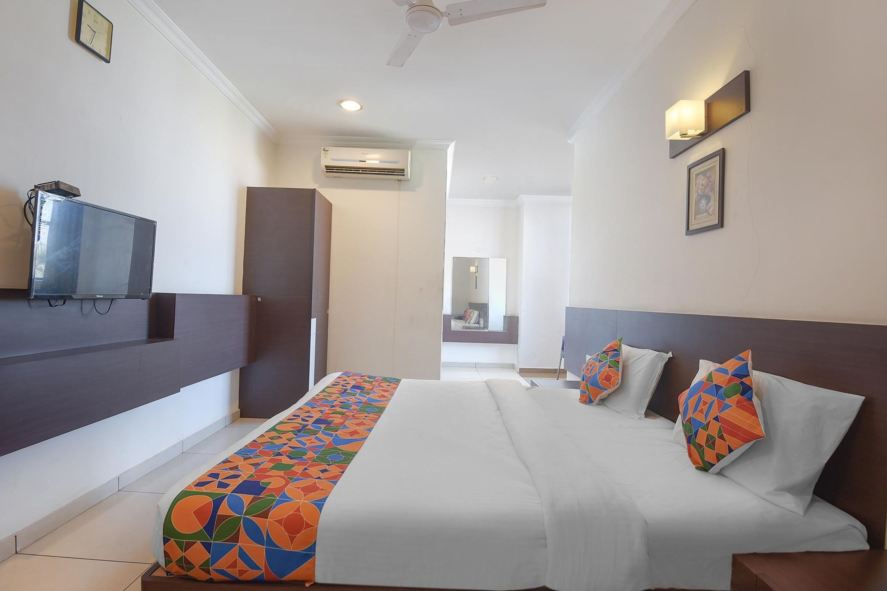 A hotel room with a bed, a television, a ceiling fan, and an air conditioning unit.