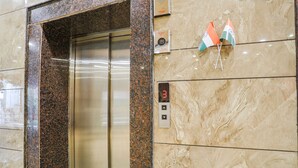 Un ascenseur doté d’un écran numérique affichant le chiffre 3, deux drapeaux indiens et un mur en marbre.