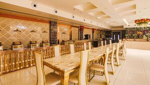 Un vaste espace dédié à la salle à manger, avec une longue table en marbre et des chaises dorées, un mur recouvert de carreaux décoratifs et un plafond orné.