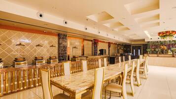 A spacious dining area with a long marble table and gold chairs, a tiled backsplash, and a decorative ceiling.
