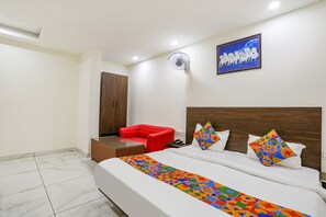 Ein Hotelzimmer mit einem großen Bett, einem roten Sessel, einem Holzkopfteil, einem Wandventilator und einem Gemälde.