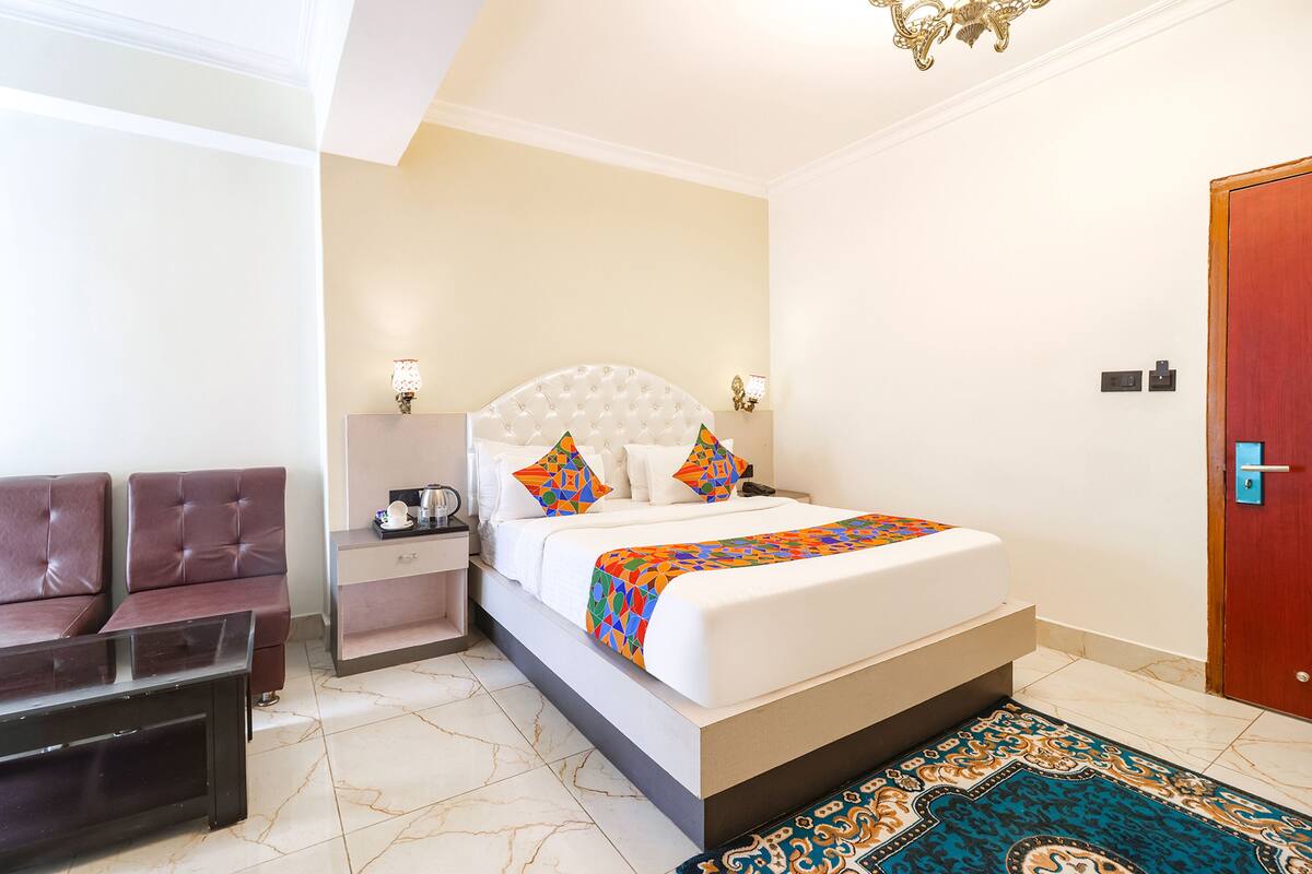 A hotel room with a large bed, a nightstand, a seating area, and a door.
