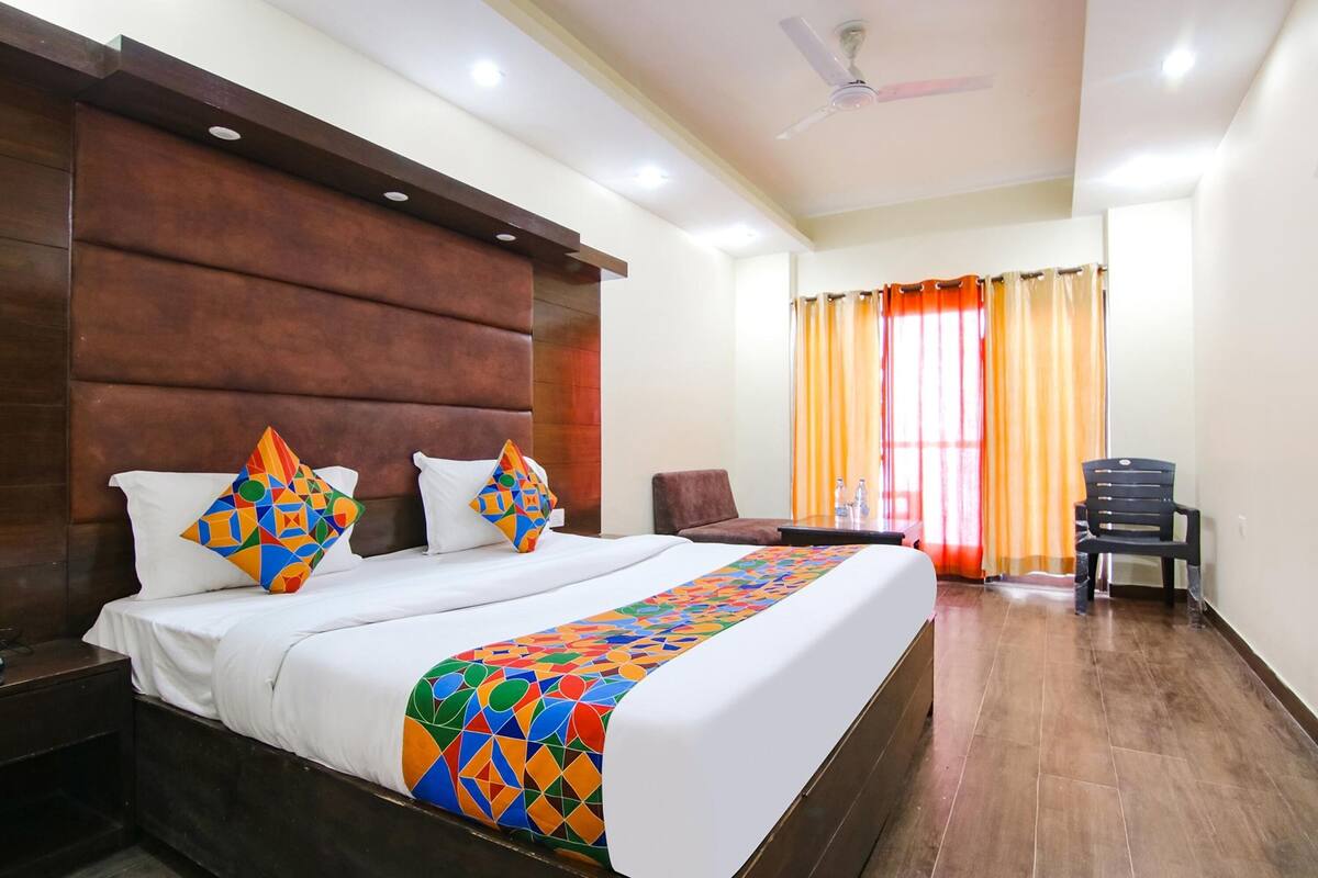 Habitación de hotel con una cama grande, cabecera de madera, escritorio, silla y ventana con cortinas.