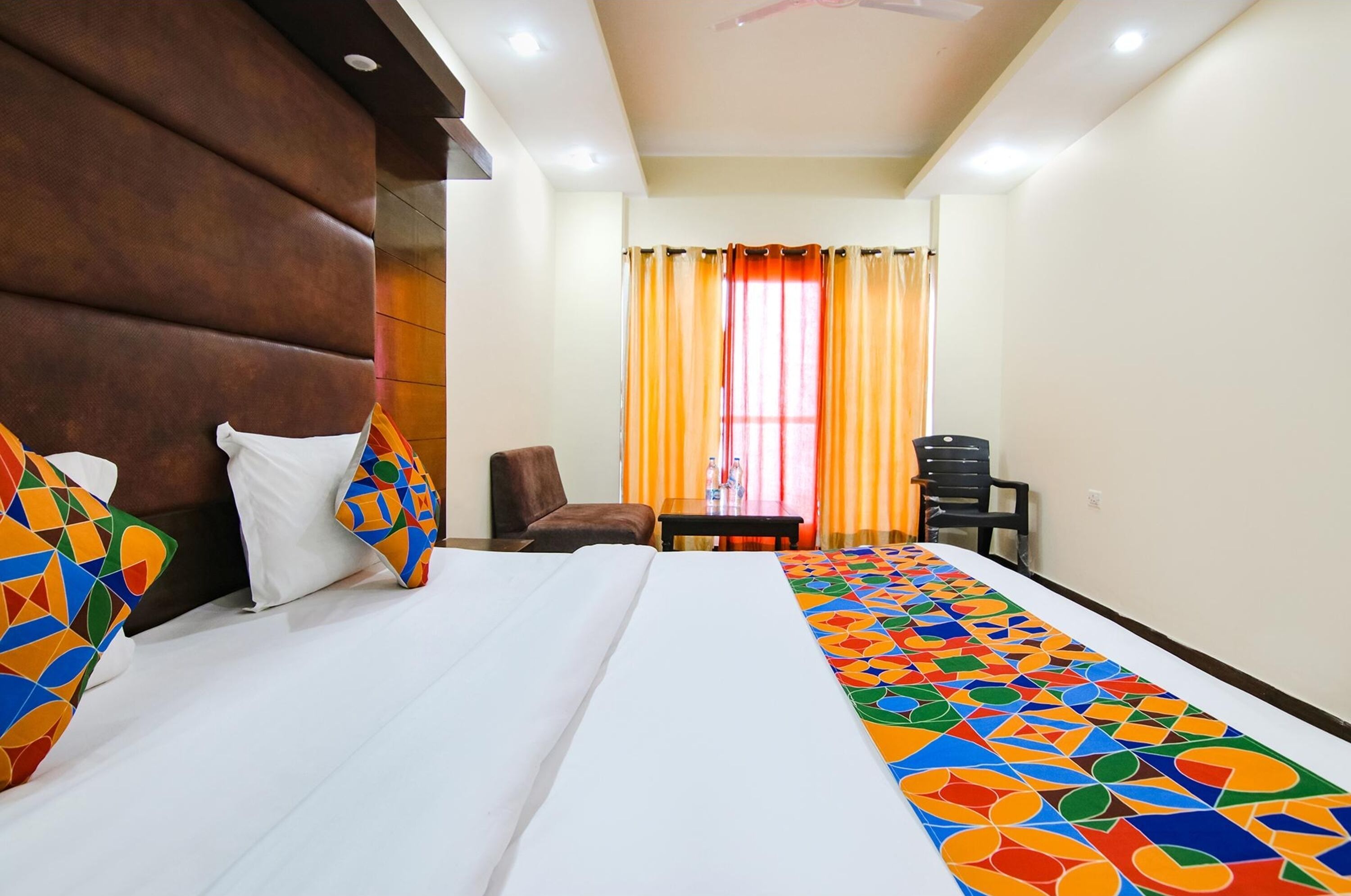 A hotel room with a large bed, a small table, a chair, and a window with curtains.