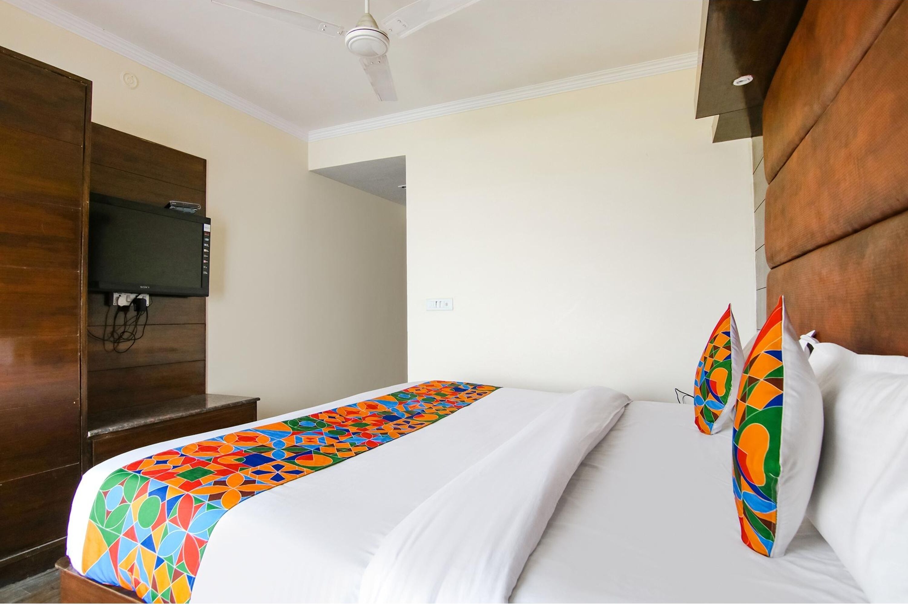 Een hotelkamer met een bed, een aan de muur bevestigde televisie en een plafondventilator.
