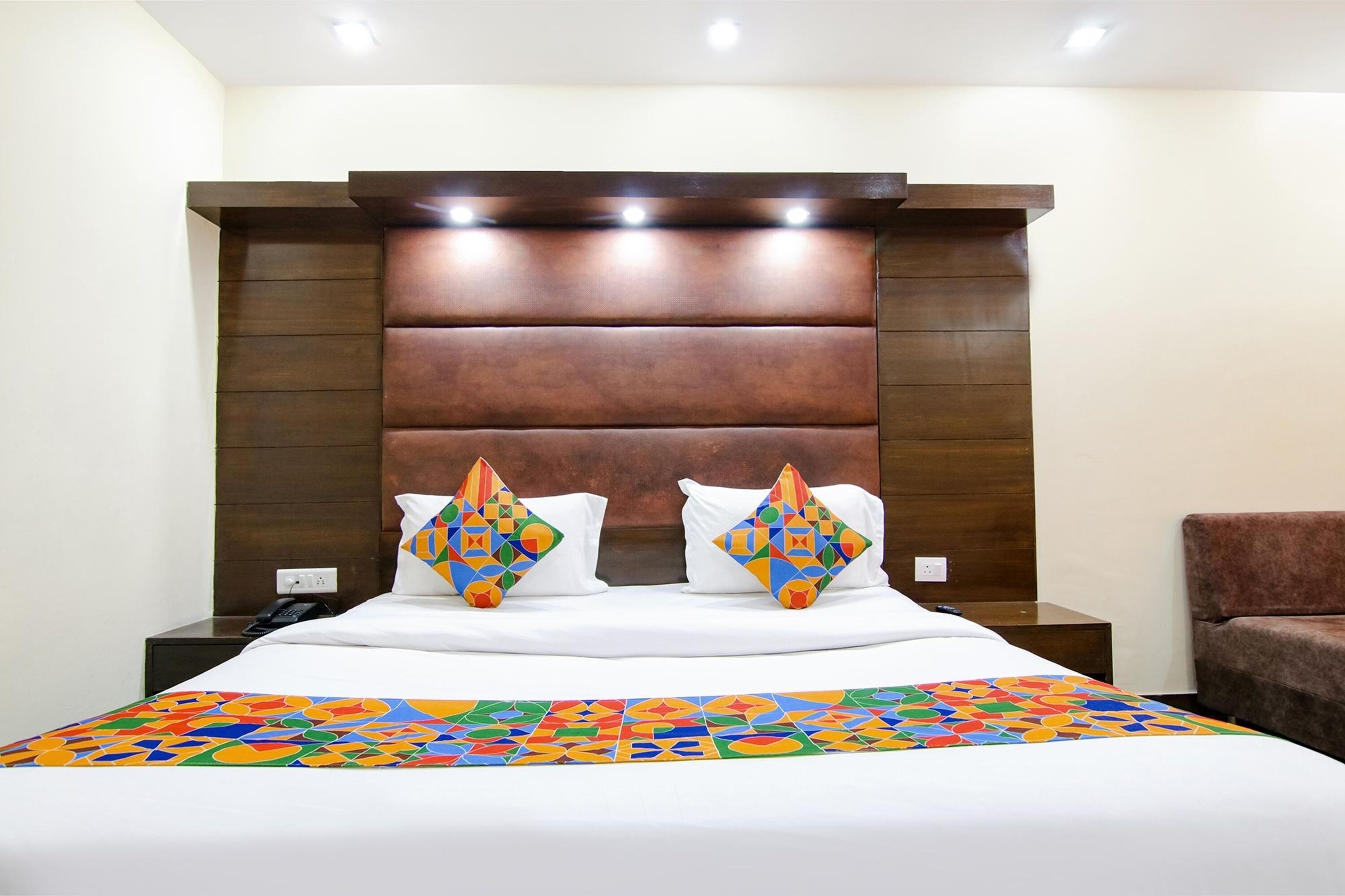 A hotel room with a large bed, two decorative pillows, a nightstand, and a brown armchair.