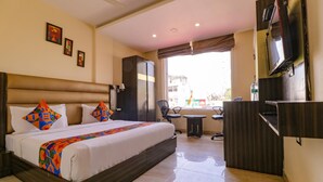 A hotel room with a large bed, a desk with a chair, a television, and a wardrobe. - Fabhotel Narula (Dehradun)