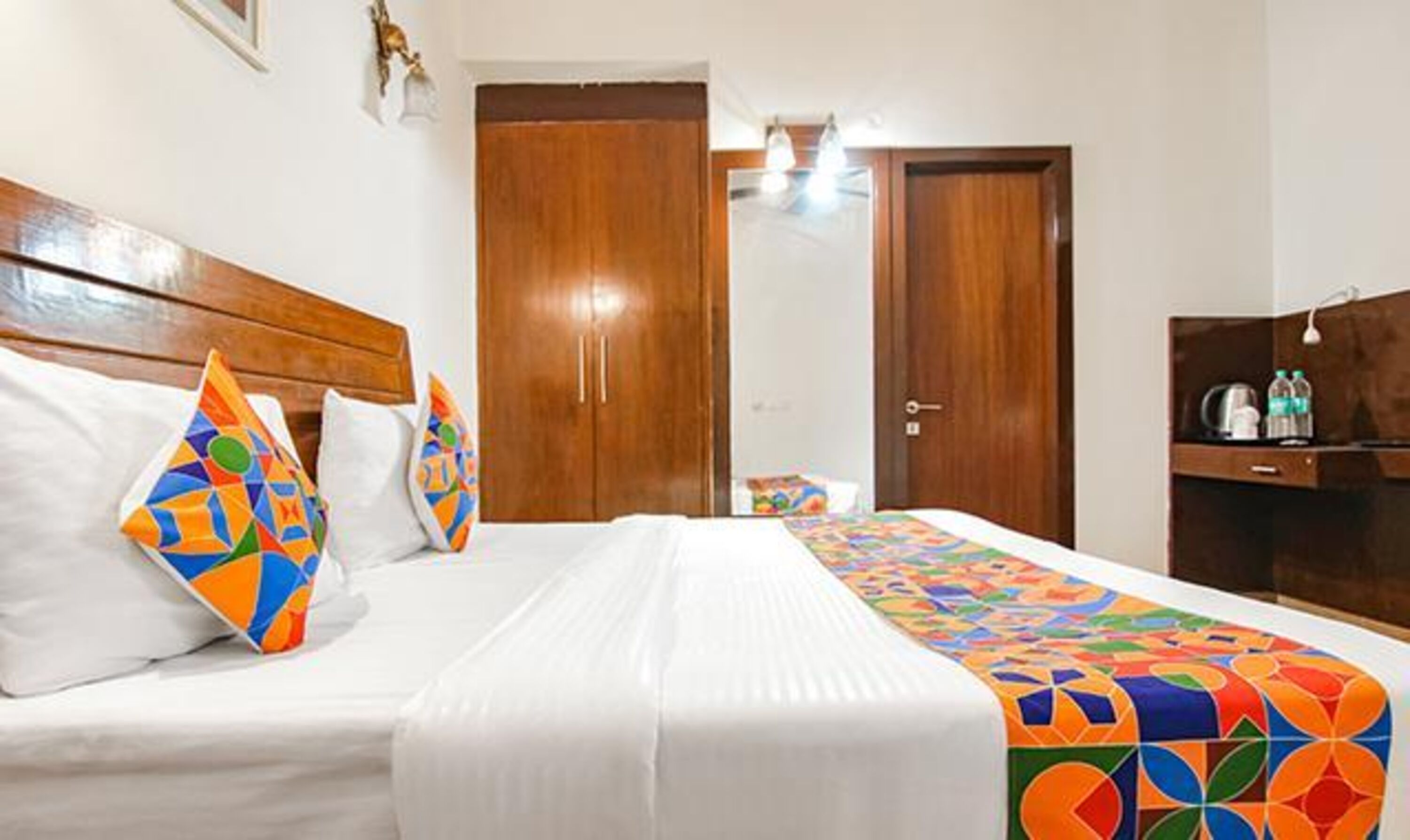 A hotel room with a bed, two wooden wardrobes, a desk with a kettle, and a nightstand.