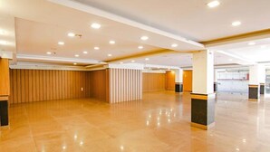 A spacious, well-lit indoor area with a polished floor, wooden paneling on the walls, and a series of columns with black and gold accents. - Fabhotel The Green Majestic (Dehradun)