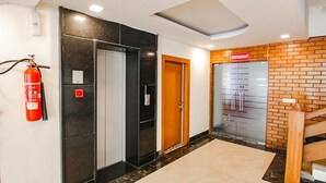 A hotel lobby with a fire extinguisher, a wooden door, and a glass wall with a sign. - Fabhotel The Green Majestic (Dehradun)
