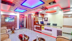 A modern hotel lobby with a reception desk, seating area, and a large TV screen displaying a scenic view. - FabHotel The Crown Comforts (Bidhannagar)