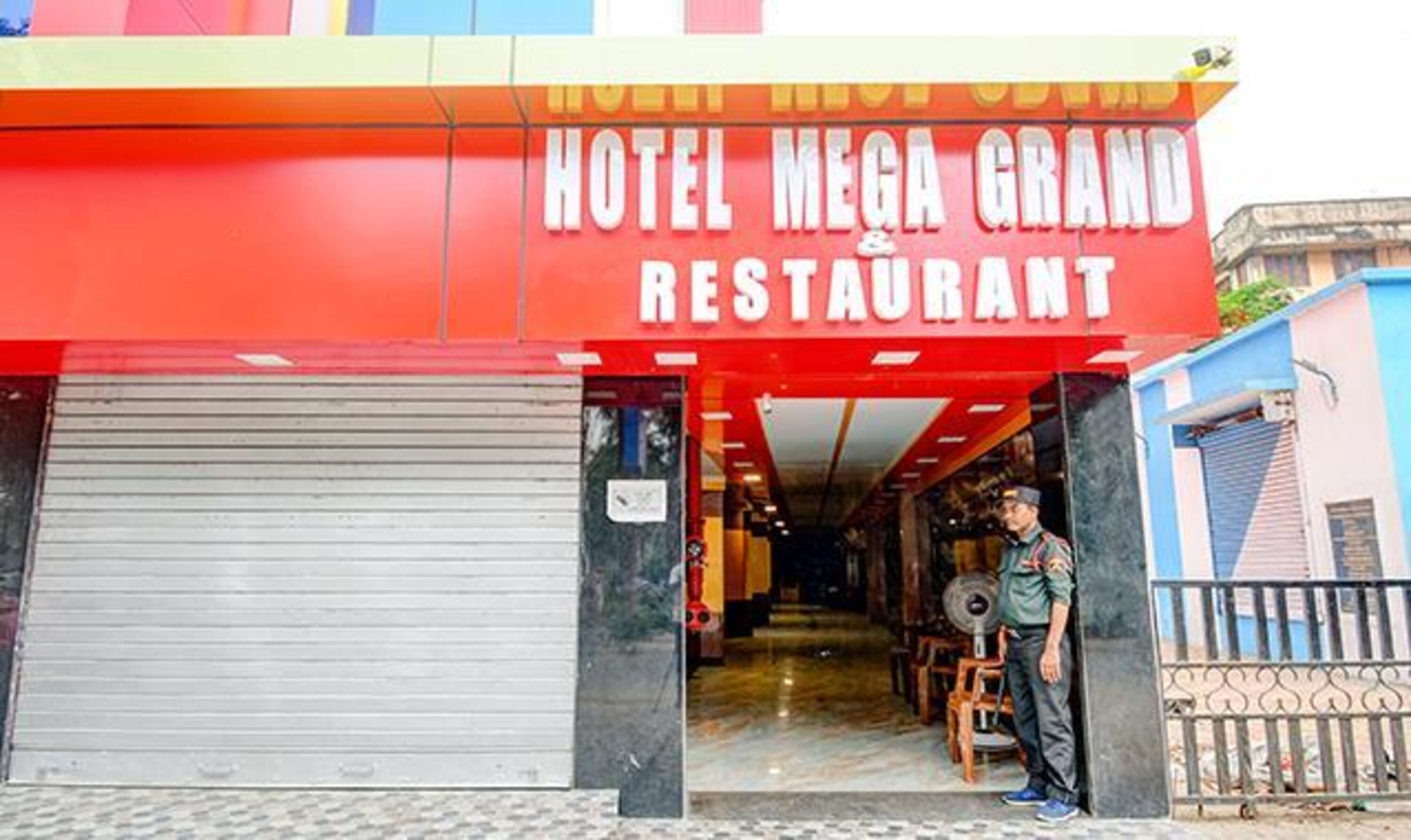 Der Eingang vom Hotel Mega Grand Restaurant mit heruntergelassenem Rollo und einer Person darin.