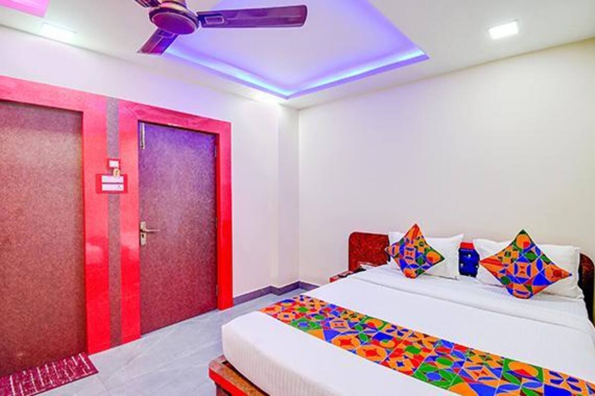 A hotel room with a bed, pillows, a ceiling fan, and a red door.