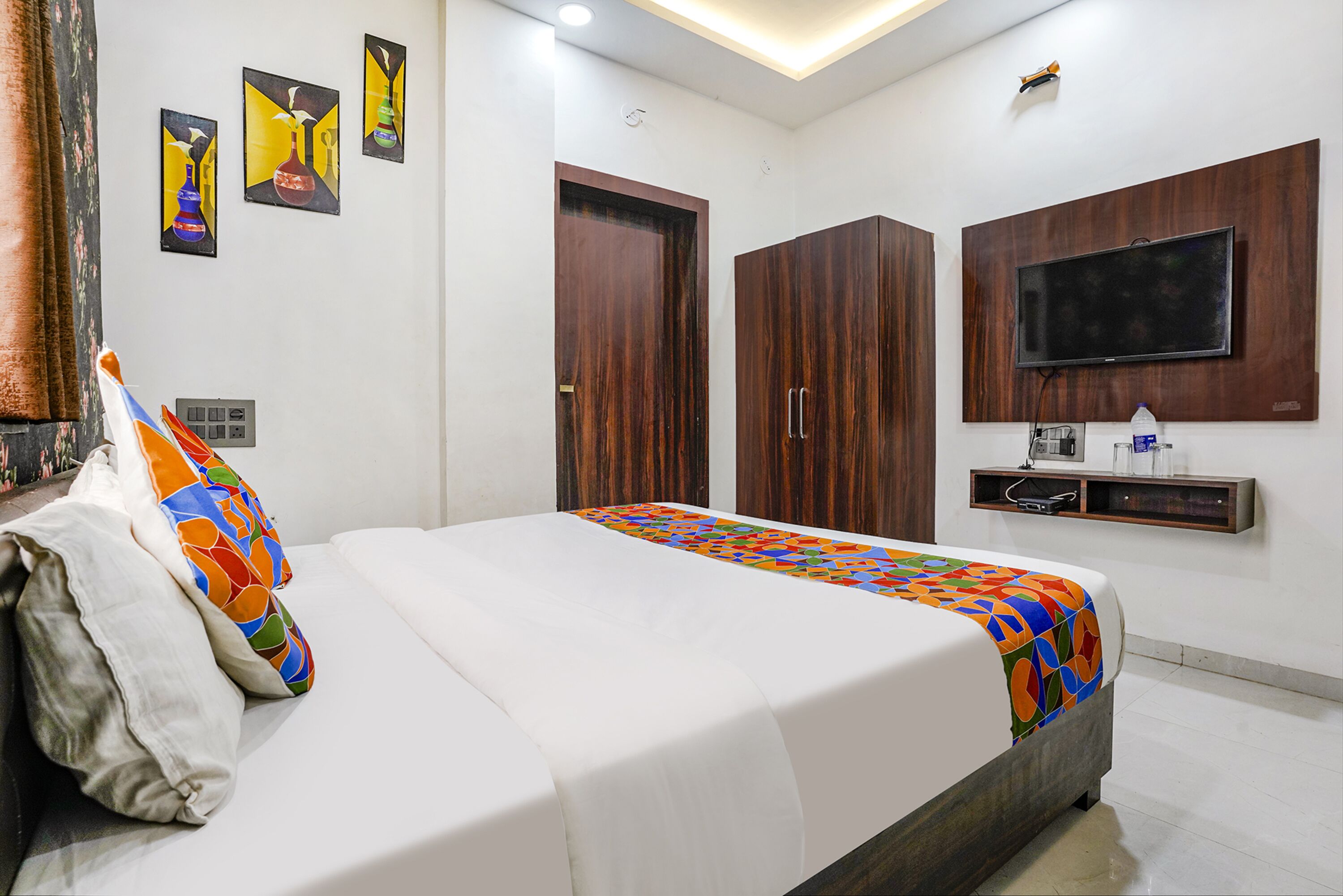 A hotel room with a bed, a TV mounted on the wall, and a wooden wardrobe.