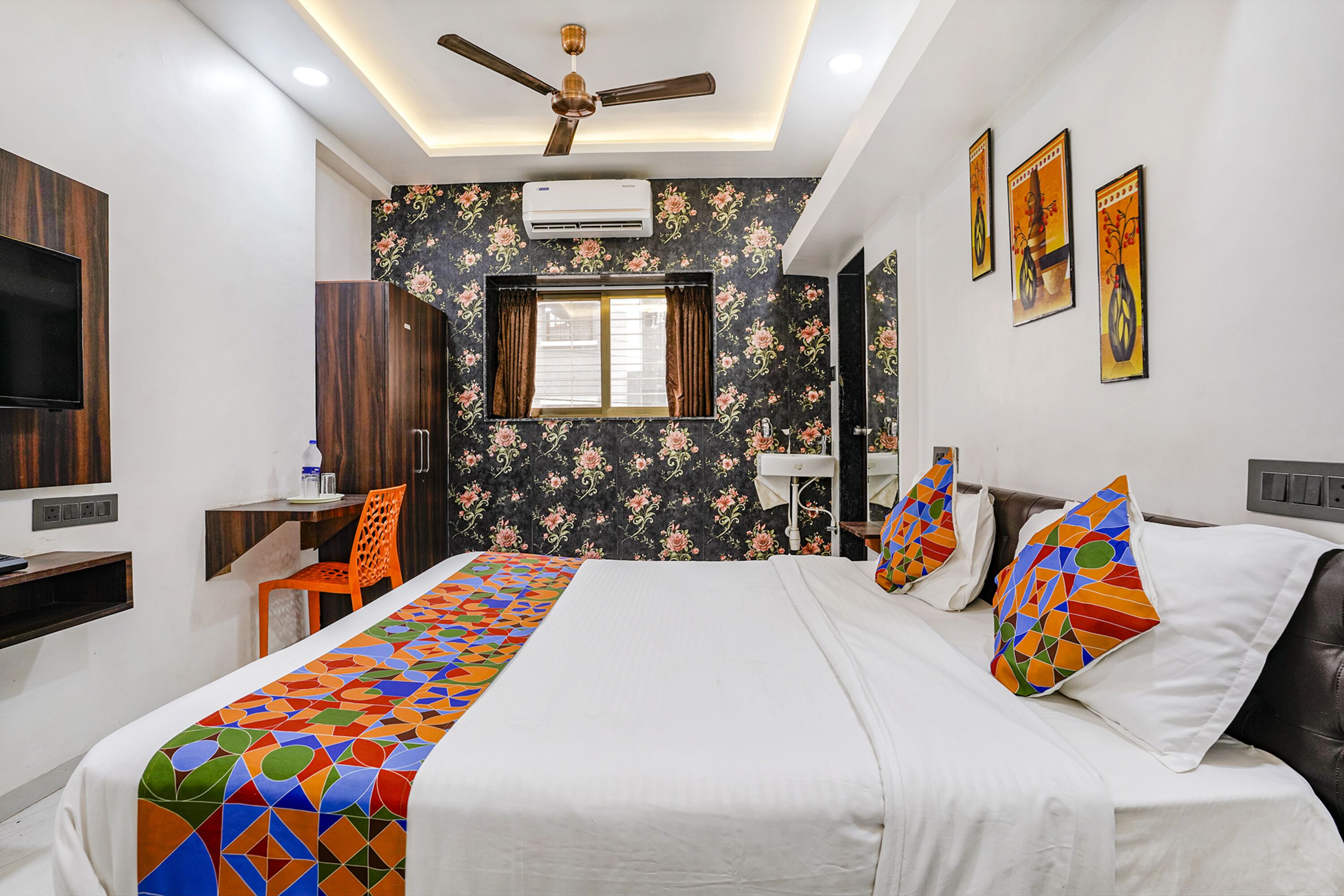 A hotel room with a bed, a desk, a chair, a TV, and a ceiling fan.