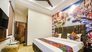 Ein Hotelzimmer mit Bett, kleinem Tisch, Sessel, Fernseher und einer Wandmalerei einer Stadtansicht.
