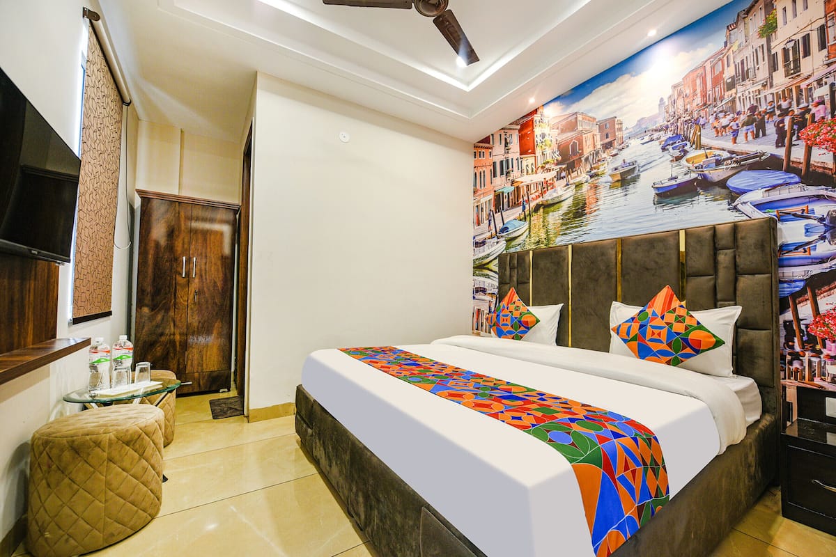 A hotel room with a bed, a small table, a chair, a TV, and a wall mural of a cityscape.
