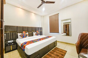 A modern hotel room with a large bed, a nightstand, a brown leather chair, a ceiling fan, and a window with a view.