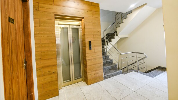 Eine Hotelhalle mit einem hölzernen Aufzug, einer Treppe mit Metallgeländern und einem gefliesten Boden.