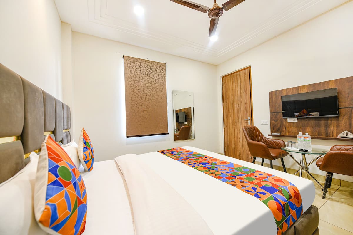 A hotel room with a bed, a TV mounted on the wall, a desk with chairs, and a ceiling fan.