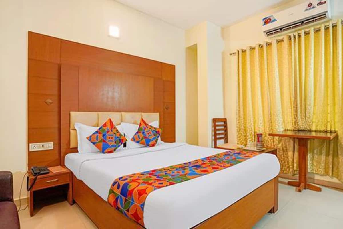 Habitación de hotel con cabecera de madera, cama con ropa de cama colorida, mesita de noche, una silla y una pequeña mesa con lámpara.