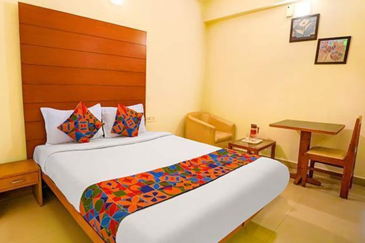 Habitación de hotel con cabecera de madera, cama con ropa de cama colorida, una pequeña mesa con una silla y dos cuadros en la pared.
