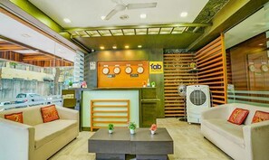 A hotel lobby with a reception desk, sofas, a coffee table, and a fan.