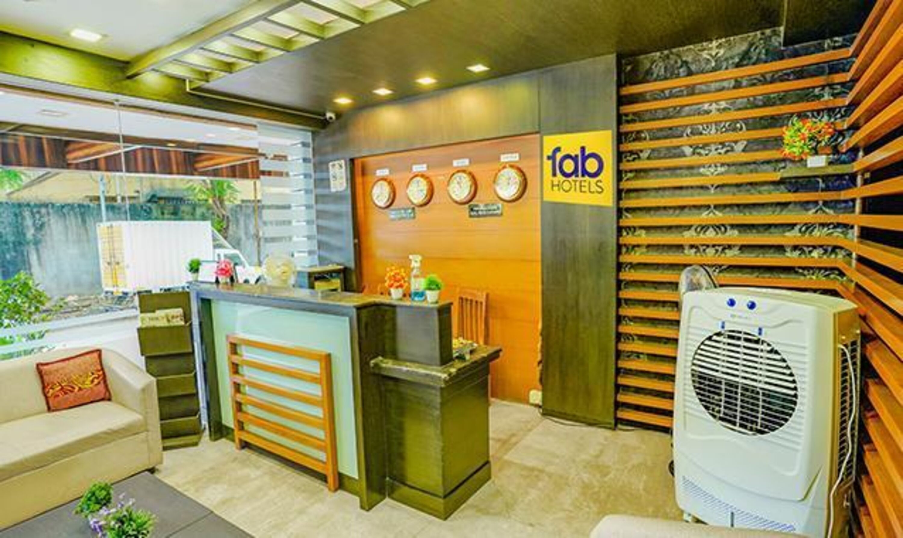 A hotel reception area with a reception desk, a sofa, a clock, and a wall-mounted air conditioning unit.