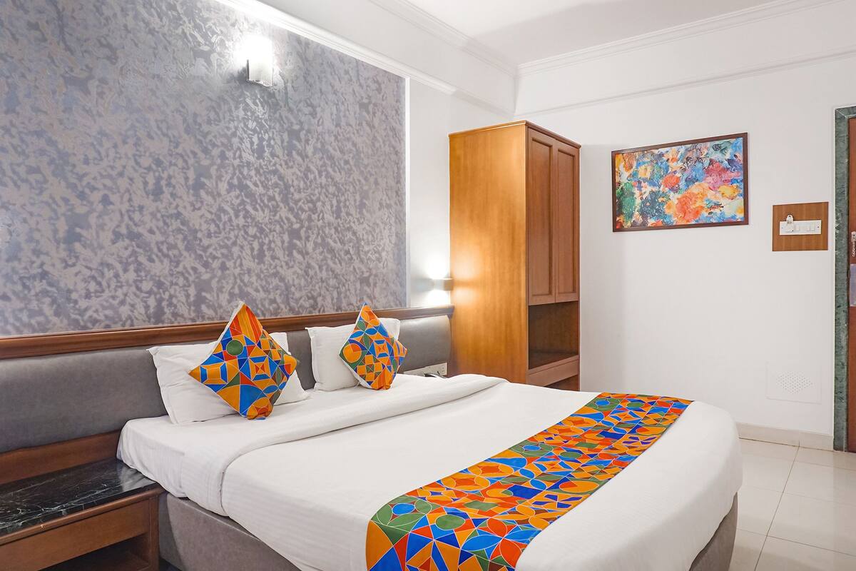 A hotel room with a bed, a nightstand, a wooden wardrobe, a colorful abstract painting, and a marble-patterned wall.