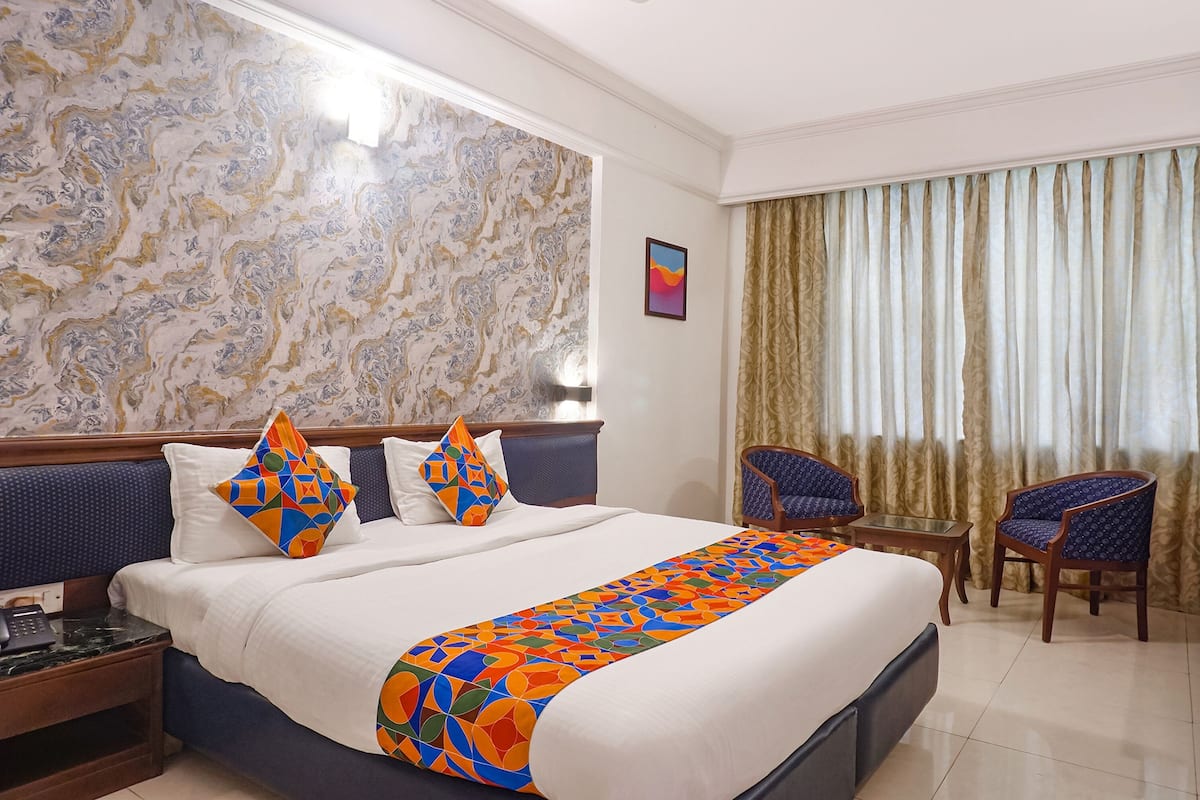 A hotel room with a large bed, two chairs, a small table, and a patterned wall.