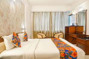Une chambre d’hôtel avec un lit, deux chaises, un bureau et un miroir.