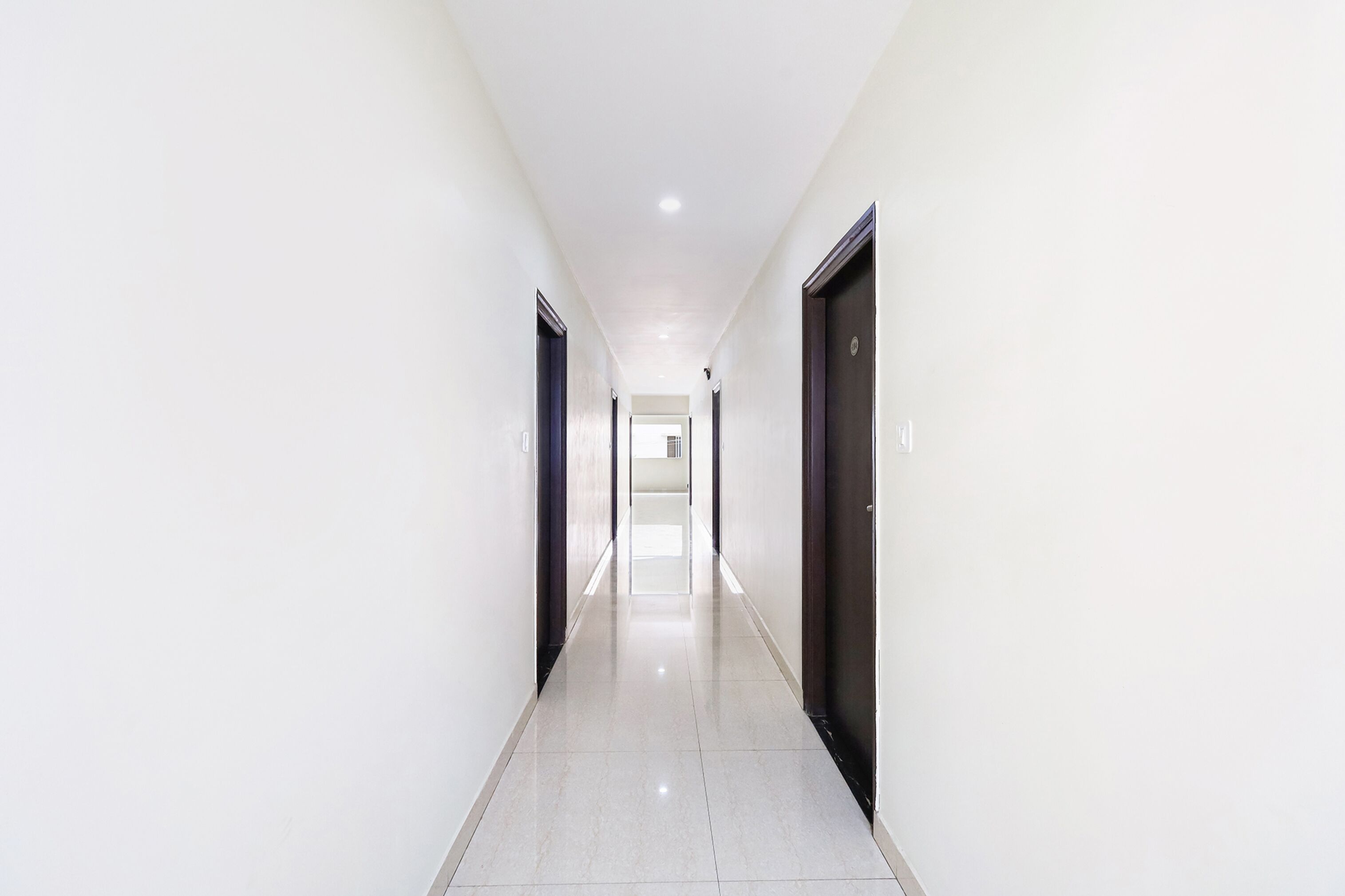 A long, narrow hallway with white walls and a shiny tiled floor, leading to a door at the end.