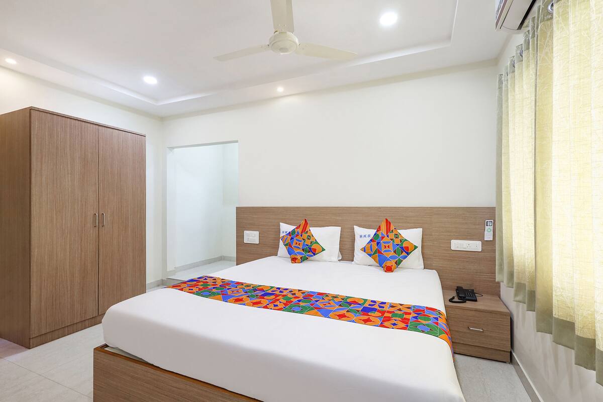 Quarto de hotel com uma cama, um guarda-roupa, uma mesa de cabeceira e um ventilador de teto.