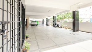 A covered parking area with a white car and a scooter parked, potted plants along the walls, and a gated entrance. - Fabhotel Karthikeya Residency (Tirupati)