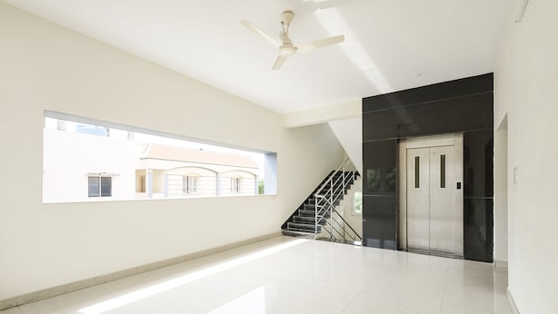 A spacious, well-lit hallway with a large window, a ceiling fan, a staircase, and a door. - Fabhotel Karthikeya Residency (Tirupati)