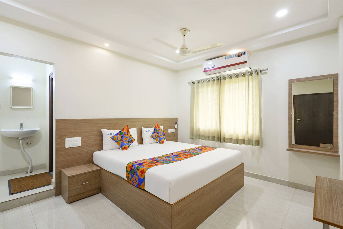 Quarto de hotel moderno com uma cama grande, mesa de cabeceira, guarda-roupa embutido e uma pequena escrivaninha.
