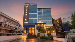 Exterior do hotel Nashik Inn com fachada moderna, uma placa de identificação em destaque e entrada bem iluminada.