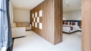 Quarto de hotel moderno com parede de destaque em madeira, sofá branco, cama com almofadas coloridas e uma grande janela com cortinas.